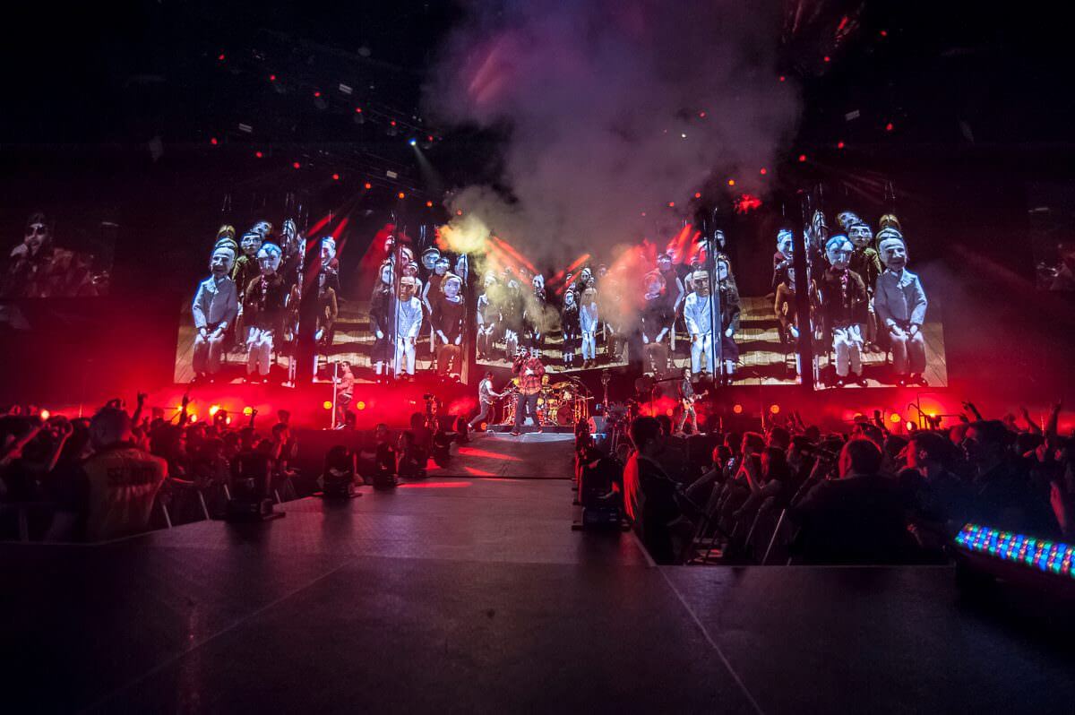 Avenged Sevenfold manggung dengan background boneka kertas yang sedang duduk berbaris ke belakang